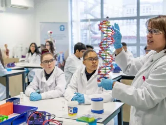 A science teacher talks to the class, holding up a model to explain something, as the school children look on